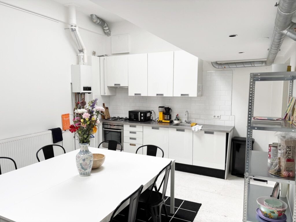 Modern white kitchen with dining table, fresh flowers in a vase, and open metal shelving.